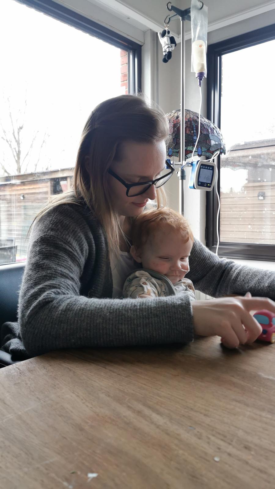 Jolien houdt baby Seth vast aan tafel met sonde-apparatuur op de achtergrond
