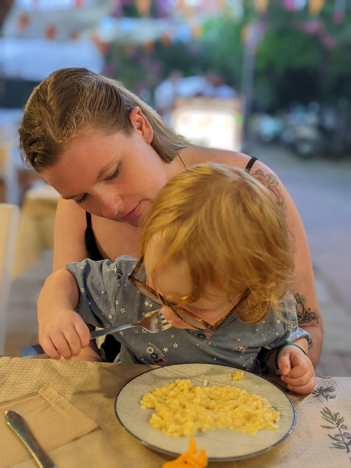 Jolien met Seth die zelf pasta eet met een vork op vakantie