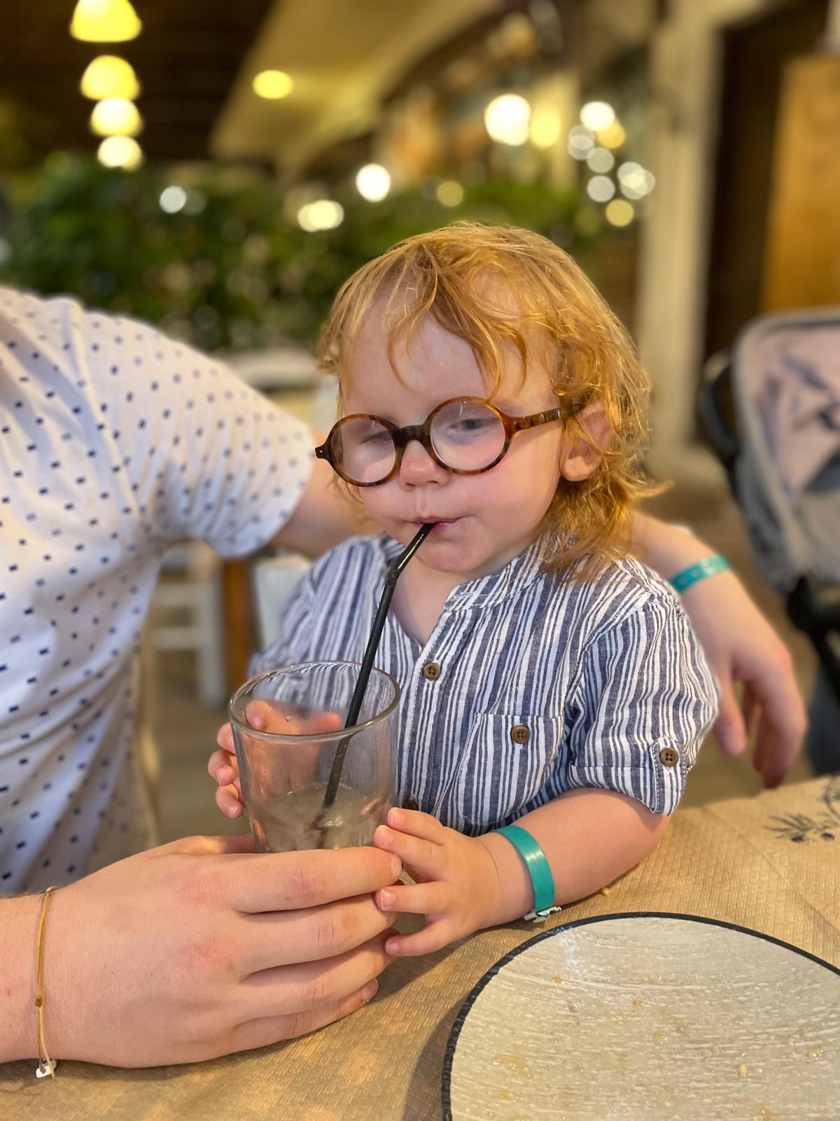 Seth drinkt met een rietje uit een glas op restaurant met zijn bril op