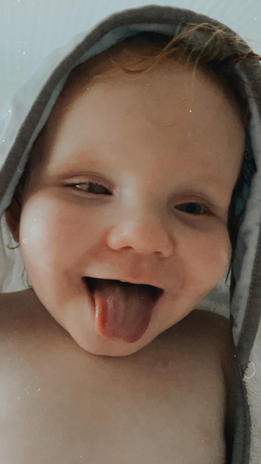 Baby Seth steekt lachend zijn tong uit in een handdoek na het bad