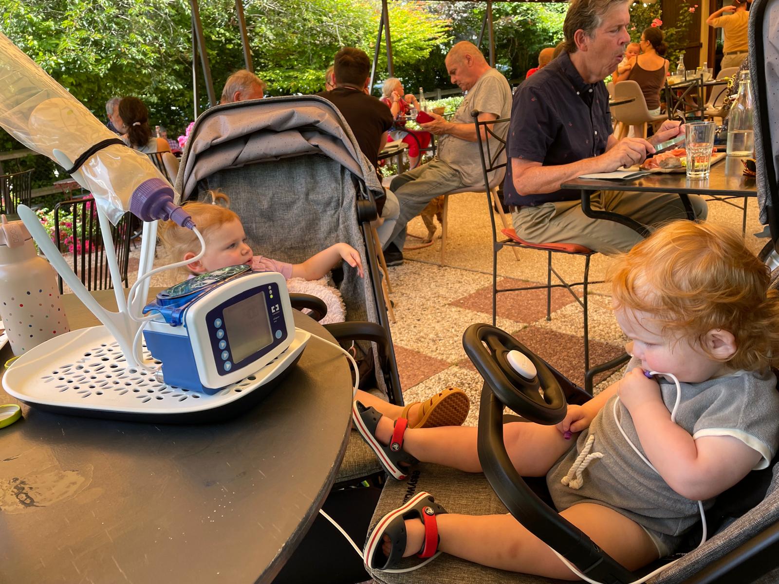 De tweeling in hun buggys op een restaurantterras met de voedingspomp ernaast