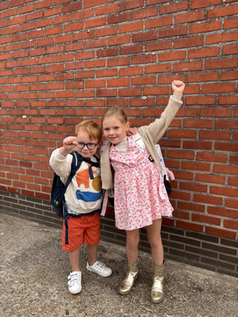 Seth en Skyler-Lily met hun boekentas aan de schoolpoort, Seth met zijn arm in de lucht